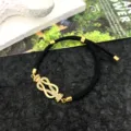 Primo piano dettagliato di un bracciale in corda nera con fibbia geometrica dorata tempestata. - Bracciale con Fibbia a Ferro di Cavallo / Corda Nera