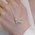 Primo piano dettagliato del ciondolo a fiocco in zircone scintillante, catena dorata. - Collana Fiocco / Oro