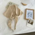 Detailed flat lay shot of a cozy beige knitted triangular scarf with decorative tie knots. - 130x24cm / Light Coffee