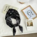 Detail view of the black floral patterned triangular headscarf with cute scalloped white lace edge. - Black