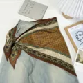 Detail view of a vintage paisley print triangle scarf styled with denim jeans and props. - Orange Coffee