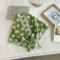 Green knitted triangle scarf detail with white heart pattern, cozy stylish accessory. - Green