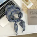 Detailed shot of a chic blue plaid triangular scarf, styled on a flat lay background. - 105 x 32 cm / Grey Blue