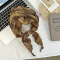 Close-up detail of the brown plaid triangle scarf, showing soft fabric and chic lettuce edge. - 105 x 32 cm / Camel