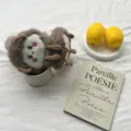 Close-up detail of the cute plush furry earmuffs displayed in a cozy aesthetic tabletop scene. - Brown