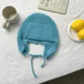 Primer plano del gorro de punto azul con orejeras y lazos sobre tela blanca con accesorios. - Talla única / Azul