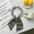 Detailed shot of plush grey neck scarf featuring plaid ribbon tail and elegant pearls. Close up. - Plaid Style