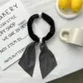 Close-up view of the stylish black plush neck scarf featuring pearl closure and striped ribbons. - Black Striped
