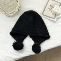 Close-up detail of black knitted balaclava hat with fluffy pom-poms, cozy texture. - One Size / Black