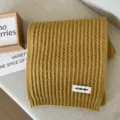Detailed view of a soft yellow knitted winter scarf with ribbed texture and woven label. - Yellow