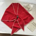 Détail d'écharpe triangulaire rouge en tricot avec coutures blanches et boucle en cuir noir. - Rouge
