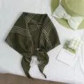 Nahansicht eines vintage dunkelgrünen Karo-Halstuchs, stilvoll arrangiert mit Strohhut als Deko. - Braun-Grün