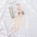 Dettaglio di nastro per capelli in chiffon con stampa floreale rosa e design elegante. - Piccolo fiore arancione