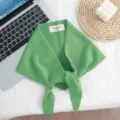 Detalle de bufanda triangular de punto de lana verde con textura suave y etiqueta de marca. - Verde