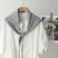 Vue detaillee d'un foulard triangulaire en tricot gris elegance sur chemisier blanc. - Gris