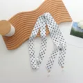 Gros plan d'une écharpe ruban en soie à pois noirs et blancs avec élégant pendentif perle. - 140x3cm / Blanc à pois