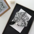 Primo piano dettagliato di foulard in seta con stampa di rose e fibbia magnetica di perle. - 50*13 cm / Stampa Rose