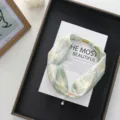Detail close up shot of a floral print silk scarf with magnetic buckle and pearl pendant. - 51*4cm / Light Green
