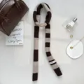 Detail shot showing the narrow striped knitted scarf in brown and beige with a woven tag. - Brown
