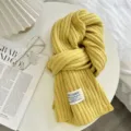 Detailansicht eines gelben Rippenstrickschals mit weicher Textur und Stoffetikett Design. - Leuchtgelb