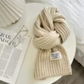 Gemütlicher, beige Strickschals-Detail mit weicher Rippenstruktur und einem Markenetikett. - Beige