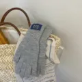 Close-up detail of cozy grey knit gloves with blue woven label, styled in a basket for winter style. - 04#-Gray