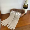 Close-up detail of cozy beige knit five-finger long gloves with cute sewn brand label tag. - Milk Tea Color