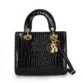 Black patent leather crocodile pattern handbag featuring top handle and gold metal charms. - Black