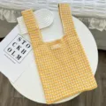 Detailed view of yellow and white striped knitted hollow out tote bag on white table scene. - Orange