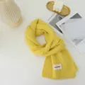 Close-up detail of the cozy yellow knitted scarf showing soft texture and brand label element. - Yellow