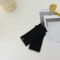 Detail view of black fingerless knit gloves with color block edges and small brand tag. - One Size / Black