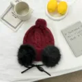 Detailansicht der winterlichen Strickmütze in Weinrot mit flauschigen Ohrenschützern und Schleife. - Einheitsgröße / Rot
