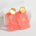 Primer plano detallado de pendientes colgantes geométricos de resina rosa y oro pulido. - Rojo Anaranjado