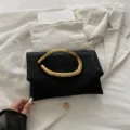 Elegant black clutch bag with unique gold sculptural handle, perfect for evening parties and events. - Black