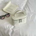 White quilted vanity bag with top handle and metal zipper charms for stylish daily use. - White
