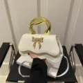 Schicke weiße Handtasche mit goldenem Griff und Schleife, ideal für elegante Damen-Outfits. - Weiß