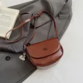 Detail shot of stylish brown leather saddle bag, elegant crossbody design with metal charm. - With Pendant / Brown