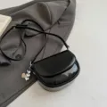 Detail view of the black patent leather saddle crossbody bag, stylish mini shoulder bag. - With Pendant / Black