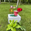 Vista ravvicinata del simpatico vaso di fiori ape in metallo su una scatola bianca all'aperto. - Ape Che Tiene una Farfalla