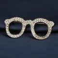 Nahaufnahme einer eleganten Brillen-Brosche in Gold mit Strass auf dunklem Stoff. - Goldene Brille Brosche