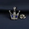 Nahaufnahme eines silbernen Kronen-Ansteckers mit klaren Strasssteinen und blauen Steinen. - Kleine Blaue Krone Brosche