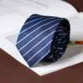 Close-up detail of a classic navy blue striped tie displayed on a stylish open book. - Hand-Tied / 8cm / Blue (A080)
