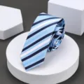 Close-up detail shot of a classic blue striped necktie displayed on white geometric block. - 6cm Cool Blue Stripe