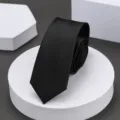 Detalle en primer plano de una corbata negra estrecha clásica enrollada en un soporte. - 6cm Negro Brillante