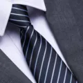 Detailed view of mens business dark blue tie with light blue stripes, paired with shirt and suit. - W2 Zipper Style / 8cm
