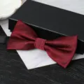 Detail view of a burgundy red men's formal bow tie with black gift box packaging and texture. - Deep Wine Red Jacquard Bowtie