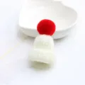 Detailed close-up of cute white knitted mini hat brooch with red pom-pom charm decoration. - White