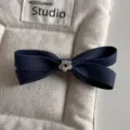 Denim bow hair clip detail view, showcasing dark blue fabric texture and a cute silver flower charm. - Bow Clip / Denim Blue