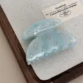 Detail close-up of a light blue translucent acetate hair claw clip embellished with stones. - Blue
