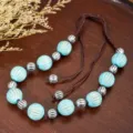 Close-up detail of retro turquoise beaded necklace with silver metal accents and brown cord. - Blue Faux Turquoise Drum Bead with Silver Striped Metal Bead Style (C23-570)